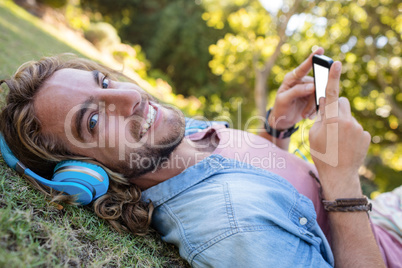 Happy man lying on grass listening to music on mobile phone