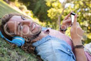 Happy man lying on grass listening to music on mobile phone