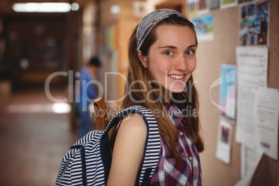 Portrait of smiling schoolgirl standing near notice board in corridor