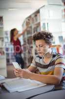 Attentive schoolboy using mobile phone while studying in library