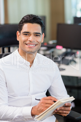 Smiling business executive writing on notebook in office