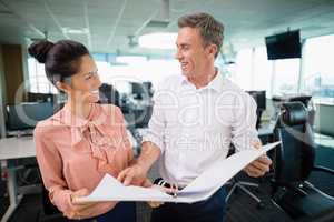 Smiling business colleagues discussing over clipboard at desk