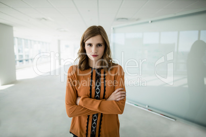 Business executive standing with arms crossed in office corridor