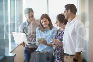 Smiling business colleagues using mobile phone, digital tablet and laptop