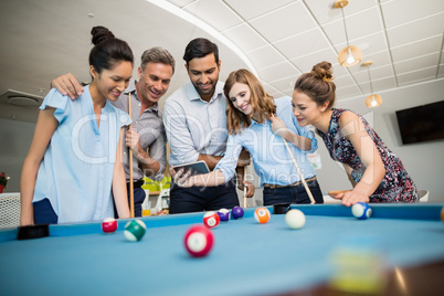 Business colleagues using mobile phone while playing pool in office space