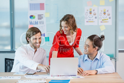 Smiling business colleagues discussing over laptop in conference room