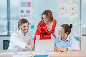 Smiling business colleagues discussing over laptop in conference room