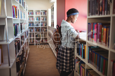 Attentive schoolgirl reading book in library