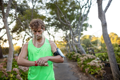 Jogger listening to music on mobile phone and checking his smartwatch