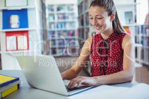 Happy schoolgirl using laptop in library