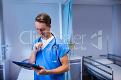 Smiling doctor writing on clipboard in ward