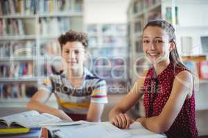 Portrait of happy schoolgirl sitting with her classmate in library