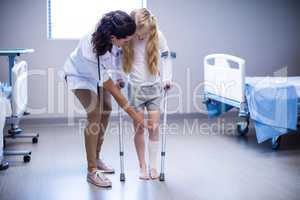 Female doctor assisting girl to walk with crutches in ward