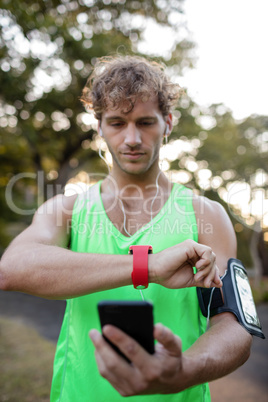 Jogger listening to music on mobile phone and checking his smartwatch