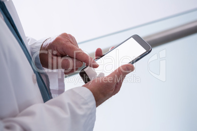 Doctor holding smartphone in the passageway at hospital