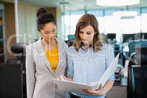 Smiling business colleagues discussing over clipboard at desk