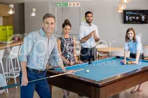 Smiling business colleagues playing pool in office space
