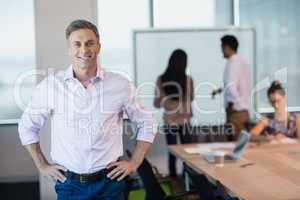 Portrait of smiling business executive standing with hands on hip in conference room
