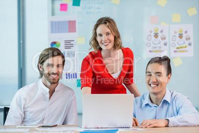 Smiling business colleagues discussing over laptop in conference room