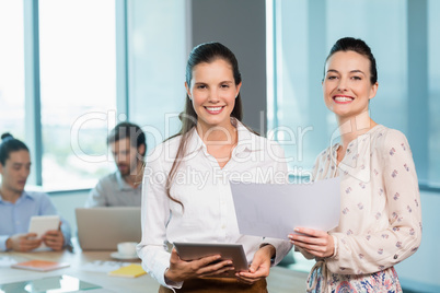 Female business executives standing with document and digital tablet in conference room