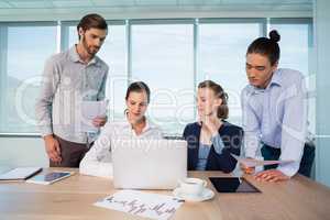 Business executives discussing over laptop in conference room