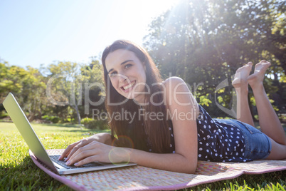 Smiling woman lying on mat and using laptop