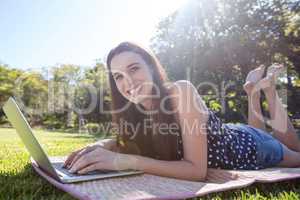 Smiling woman lying on mat and using laptop