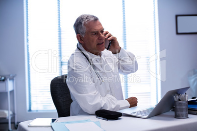 Doctor talking on mobile phone while using laptop