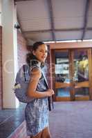 Happy schoolgirl standing with schoolbag in school campus