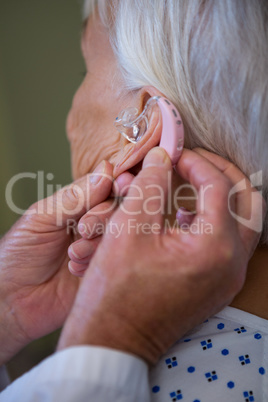 Doctor inserting hearing aid in senior patient ear