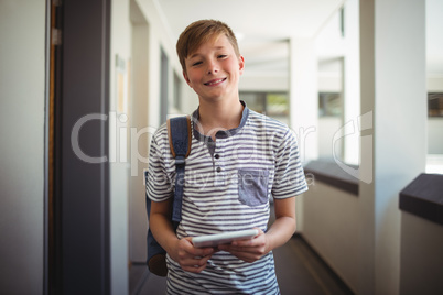 Happy schoolboy using digital tablet in corridor at school