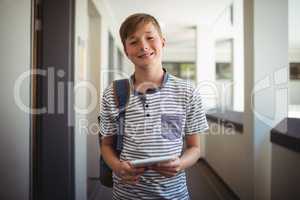 Happy schoolboy using digital tablet in corridor at school