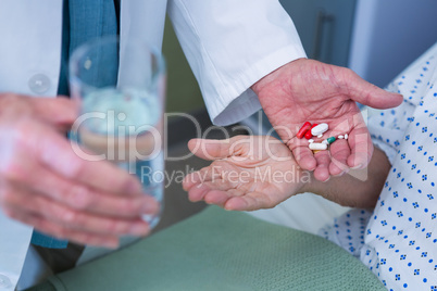 Mid-section of doctor giving medicine pill to patient
