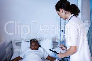 Female doctor writing on clipboard while patient lying on bed