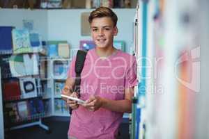 Portrait of happy schoolboy holding digital tablet in library