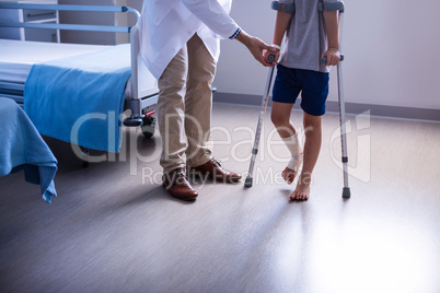 Doctor assisting injured boy to walk with crutches