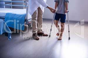 Doctor assisting injured boy to walk with crutches