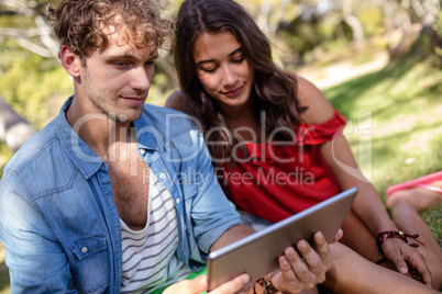 Couple sitting on grass and using digital tablet