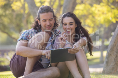 Couple sitting on grass and using digital tablet