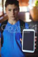 Schoolboy standing with schoolbag showing mobile phone near staircase at school