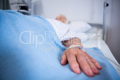 Senior patient hand with saline on bed in hospital