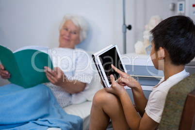 Senior patient reading a book while boy using digital tablet