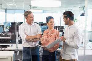 Smiling business colleagues discussing over clipboard at desk