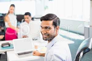 Portrait of smiling business executive working on laptop at desk