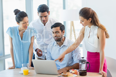 Smiling business colleagues discussing over laptop