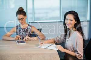 Smiling business colleagues writing on notepad and using digital tablet in conference room