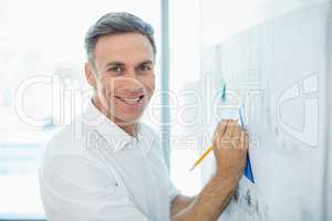 Smiling architect drawing on blueprint at whiteboard