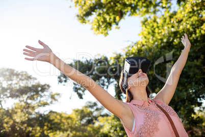 Woman raising her hands while using a VR headset in the park