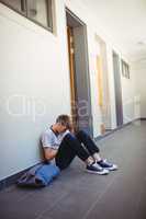 Sad schoolboy sitting in corridor