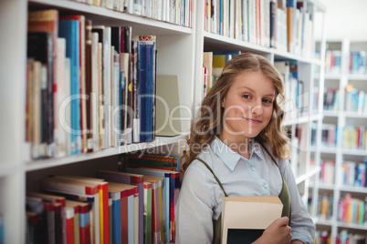 Portrait of happy schoolgirl holding book in library